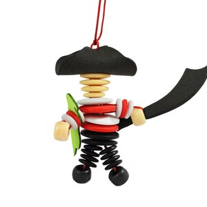 May include: A black and white pirate ornament with a red and white striped shirt, a green sword, and a black hat. The ornament is made of wood and buttons.