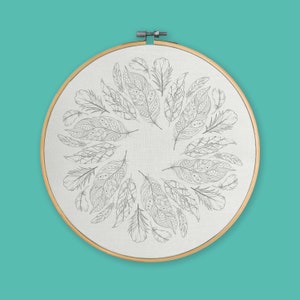 May include: A white embroidery hoop with a black and white design of feathers arranged in a circle.