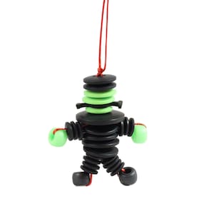 Op de afbeelding: Een zwart en groen speelgoedfiguur gemaakt van gestapelde plastic schijven. De figuur hangt aan een rood touwtje en heeft een groen hoofd en armen.