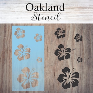 May include: A stencil with the word "Oakland Stencil" at the top and a design of multiple hibiscus flowers. The stencil is on a light blue background and is placed on a wooden surface.