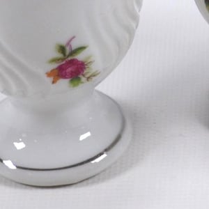 May include: Set of four white ceramic egg cups with a silver rim and a floral design featuring pink roses.