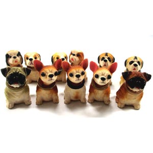 May include: A collection of small dog figurines in various breeds and colors. The figurines include pugs, chihuahuas, and other breeds, with details like collars and realistic features. The dogs are arranged in a group, showcasing their diverse appearances.