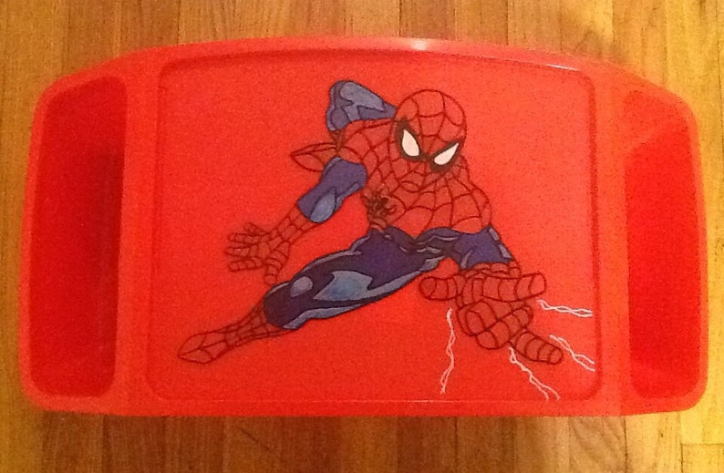 Op de afbeelding: Een felrood plastic schoottafeltje met een centrale grafische illustratie van de superheld Spider-Man in een dynamische gehurkte houding. Het personage is afgebeeld in een rood en blauw pak met een zwart webpatroon en witte ogen.
