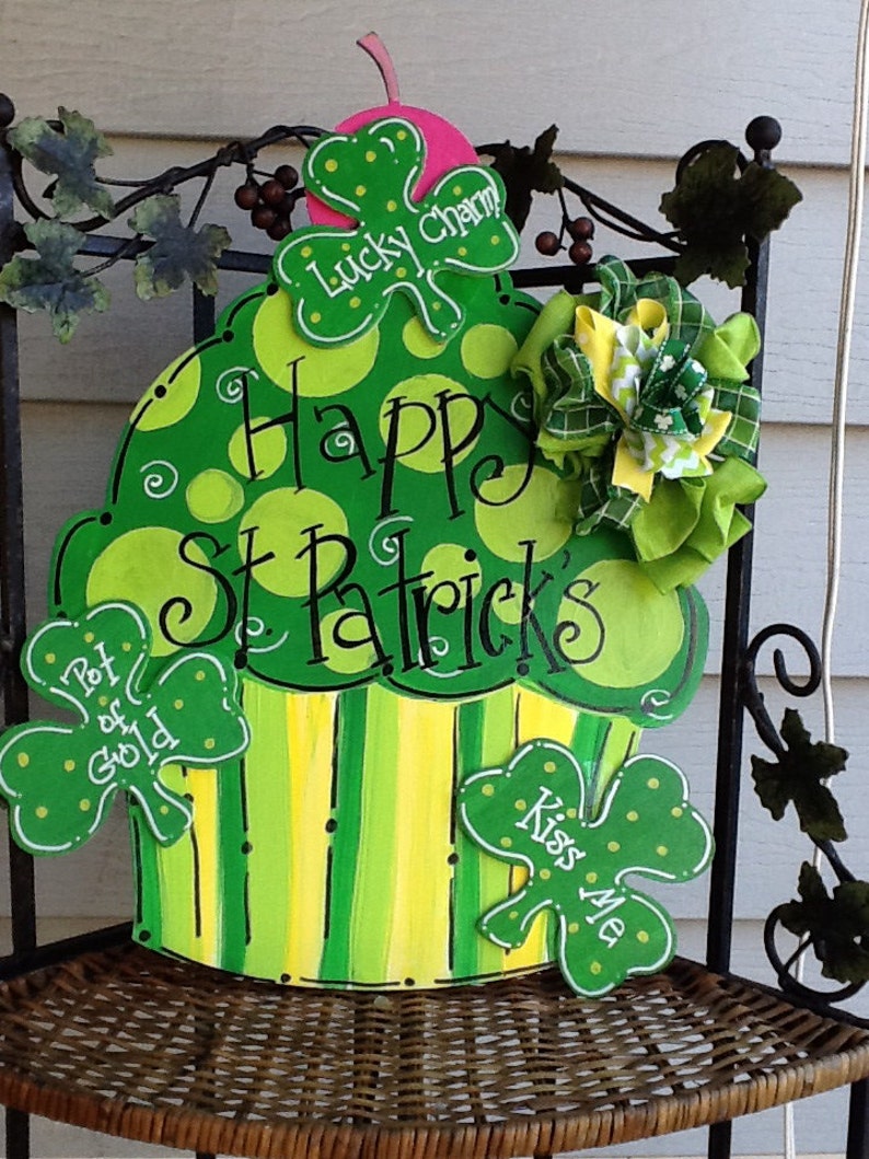 Puede incluir: Un letrero de madera con forma de cupcake verde y amarillo con lunares y rayas. Incluye tres recortes de tr&eacute;bol con el texto Lucky Charm, Pot of Gold y Kiss Me, adem&aacute;s del texto Happy St Patrick's y un lazo de tela verde y amarillo.