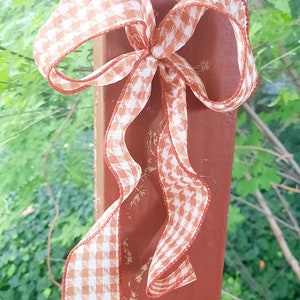 May include: A decorative bow made of orange and white gingham ribbon with wired edges. The bow features two loops and two long, trailing tails. The text "2 loop" is printed in black on the surface behind the ribbon, indicating the style.