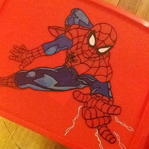 Op de afbeelding: Een felrood rechthoekig plastic deksel voor een opbergbak met een grafische illustratie van de superheld Spider-Man in een dynamische gehurkte houding. Het personage draagt een rood en blauw pak met zwarte webpatronen en witte ogen.