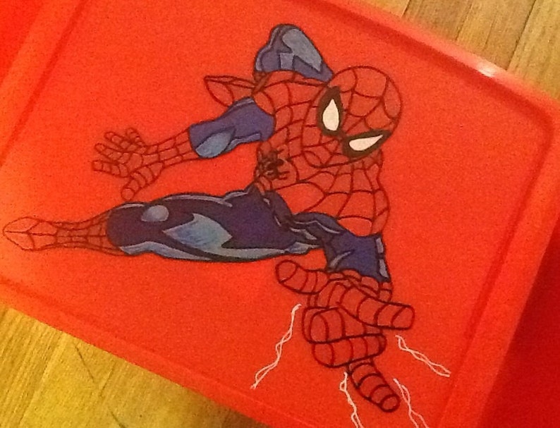 Op de afbeelding: Een felrood rechthoekig plastic deksel voor een opbergbak met een grafische illustratie van de superheld Spider-Man in een dynamische gehurkte houding. Het personage draagt een rood en blauw pak met zwarte webpatronen en witte ogen.