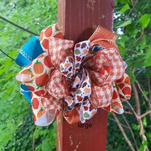 May include: A decorative bow featuring multiple ribbons with patterns of orange pumpkins, orange and white gingham, and colourful autumn leaves, accented by solid teal ribbon loops. The word large is printed in black text at the bottom.