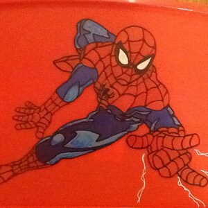 Op de afbeelding: Een rechthoekig rood plastic dienblad met een grafische illustratie van de superheld Spider-Man in een dynamische gehurkte houding. Het personage draagt een rood en blauw pak met een zwart webpatroon en witte ogen, en schiet witte webben.