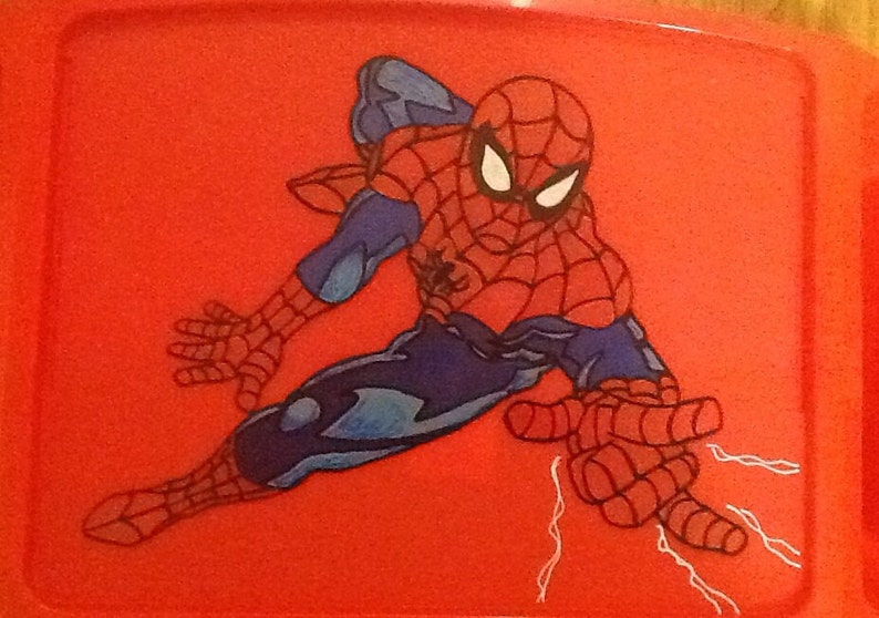 Op de afbeelding: Een rechthoekig rood plastic dienblad met een grafische illustratie van de superheld Spider-Man in een dynamische gehurkte houding. Het personage draagt een rood en blauw pak met een zwart webpatroon en witte ogen, en schiet witte webben.