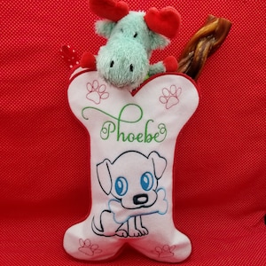 May include: White bone-shaped Christmas stocking with a red and green embroidered dog design, the name "Phoebe" embroidered in green, and a plush moose toy peeking out of the top.