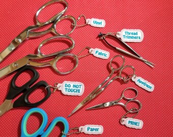 May include: A collection of ten pairs of scissors with colorful tags labeled "Vinyl", "Thread Trimmers", "Fabric", "Do Not Touch", "Applique", "Mine!" and "Paper".