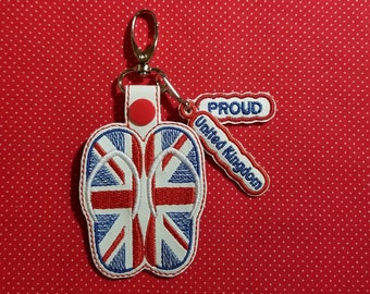 Peut inclure: Un porte-clés blanc avec une paire de tongs rouge, blanc et bleu avec le motif de l'Union Jack. Le porte-clés a également un bouton rouge et une étiquette qui dit "Fier d'être Britannique".