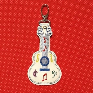 May include: White guitar-shaped keychain with colorful embroidered musical notes and a key ring.