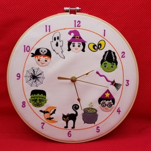 Peut inclure: Une horloge blanche avec un cadre en bois et des aiguilles noires. Le cadran de l'horloge a un thème d'Halloween avec des images brodées d'un fantôme, d'une sorcière, de Frankenstein, d'une toile d'araignée, d'un chat, d'un chaudron et d'un magicien. Les chiffres de 1 à 12 sont autour du cadran de l'horloge.