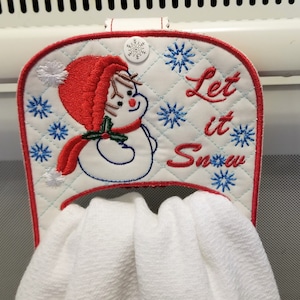Könnte beinhalten: Weißer, gesteppter Handtuchhalter mit einem roten Schneemann und dem Text "Let it Snow".