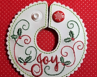 May include: White felt Christmas ornament with green and red embroidery. The ornament features the word "joy" and holly leaves. It has a hole in the center for hanging.