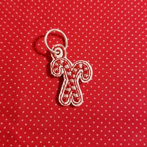 May include: A silver charm with a red and white candy cane design. The charm is attached to a silver ring.