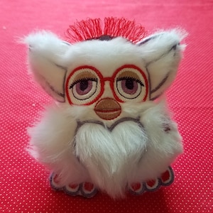 May include: White furry toy with red hair, red and white glasses, and a pink mouth. The toy is a popular children's toy.