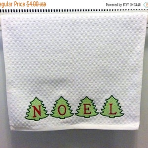 May include: White hand towel with a textured pattern. The word "NOEL" is embroidered in red letters within green Christmas tree designs. The towel is hanging on a white bar.