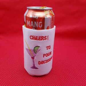 May include: White can cooler with red embroidery that says "Cheers! To Pour Decisions" and a pink cocktail glass with a lime wedge. A can of Rita's Mango is inside the cooler.
