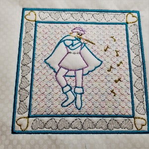 May include: Embroidered design of a person playing a flute, surrounded by a border of hearts. The background is a pattern of hearts in various colors.