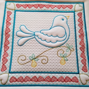 May include: A white embroidered bird with blue accents perched on a green branch with yellow pears. The bird is surrounded by a red heart border with a turquoise frame.