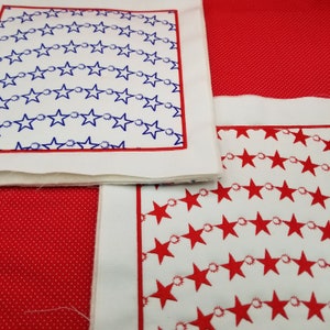 May include: Three white fabric squares with red and blue star patterns. The top square has a blue star pattern with a red border. The bottom two squares have red star patterns with red borders. The squares are sewn together to create a larger piece of fabric.