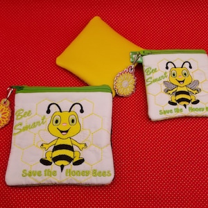 Puede incluir: Dos pequeñas bolsas con cremallera con un diseño de abeja. Las bolsas son blancas con un patrón de panal y ribete verde. Las abejas son amarillas y negras con una cara sonriente. Las bolsas tienen el texto "Bee Smart" y "Save the Honey Bees".