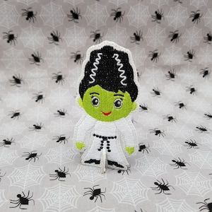May include: Green and black embroidered patch of a Frankenstein character wearing a white karate uniform with a black belt. The character has black hair with white zigzags and a green face with a smile.