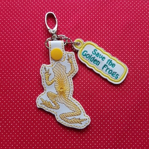 May include: White leather keychain with a gold embroidered frog and a white tag that says "Save the Golden Frogs" in green and yellow embroidery.
