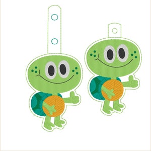 以下が含まれることがあります： オレンジ色の甲羅と笑顔の顔をした緑色の亀の形をしたキーホルダーが2つ。それぞれのキーホルダーには、バッグや鍵に取り付けるためのループが付いています。