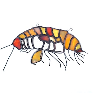 May include: A stained glass shrimp with a yellow, orange, and red color scheme. The shrimp is made of small pieces of glass that are joined together with black lead. The shrimp is hanging from a wire.