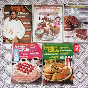 May include: A selection of vintage Family Circle magazines with vibrant covers. The magazines showcase images of food, desserts, and women. One magazine features a woman in a white sweater. A small red box is also present.