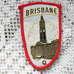 May include: Red and white embroidered patch with the text "BRISBANE" in gold lettering. The patch features a gold embroidered image of a building with a clock tower.