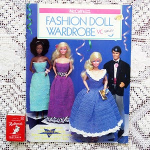 May include: A vintage McCall's Fashion Doll Wardrobe pattern book with illustrations of dolls in gowns and a tuxedo. The cover is blue with white and pink text. A box of Redheads matches is in the lower left corner.