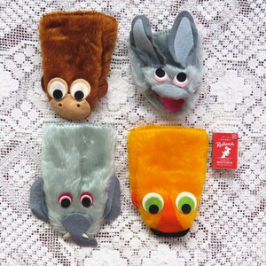 May include: Four novelty hand puppets with animal faces: a brown monkey, a grey bunny, a grey elephant, and an orange fish. A small box of Redheads matches is also present. The puppets have large eyes and are set against a white lace background.