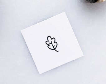 May include: A close-up of a white card with a black outline of an oak leaf. The card is on a white surface.