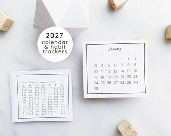 May include: A set of white paper cards featuring a 2027 calendar and habit trackers. One card displays the month of January with a grid of dates, while another shows a weekly habit tracking grid with checkboxes. Text reads 2027 calendar & habit trackers.