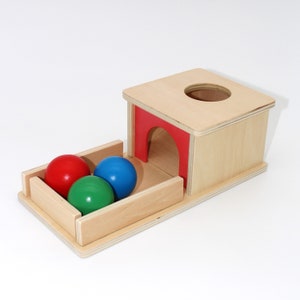 May include: A wooden toy with a red, blue, and green ball. The balls are in a tray that slides out from under a wooden box with a red opening.