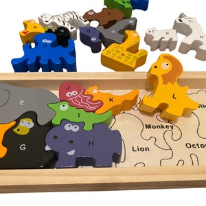 May include: A wooden puzzle with colorful animal pieces and letters. The puzzle pieces are arranged in a wooden frame with the names of the animals printed below each piece. The animals include an elephant, a hippopotamus, a lion, a monkey, an octopus, a rhinoceros, a jellyfish, and a giraffe.