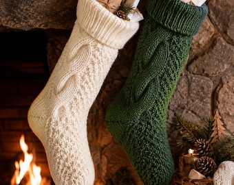 May include: Two knit Christmas stockings, one cream and one dark green, featuring a cable knit pattern and a folded cuff. The cream stocking contains small wrapped gifts, while the green stocking holds a white gift box with a gold bell ornament.