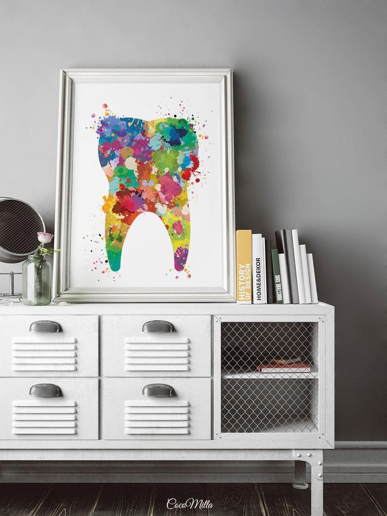 May include: A framed print featuring a colorful watercolor illustration of a tooth. The tooth is filled with vibrant splashes of red, yellow, green, blue, and purple. The artwork is displayed on a white cabinet with books and a decorative mirror.