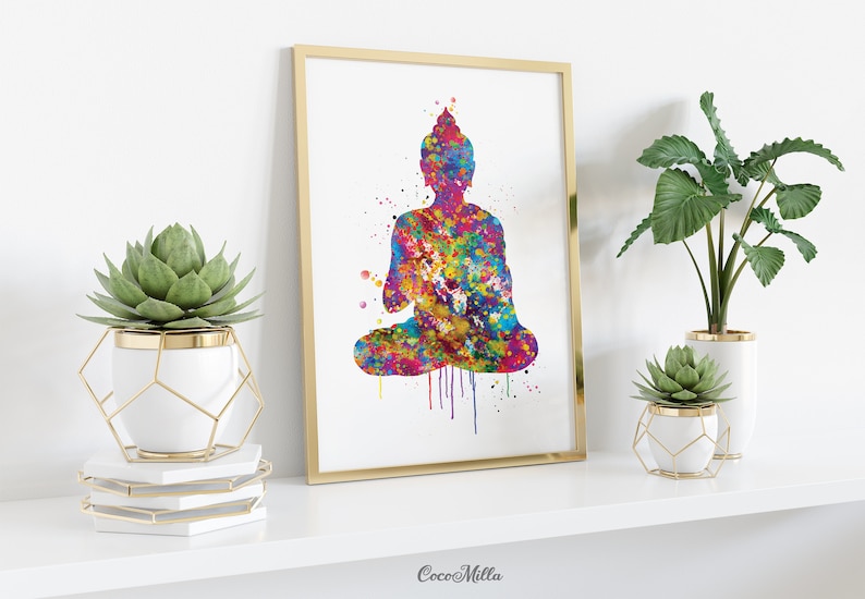 May include: A framed watercolor print of a seated Buddha figure. The artwork features a vibrant, multicolored splatter effect, with hues of blue, yellow, pink, and purple. The frame is gold, and the print is displayed on a white shelf with decorative plants.
