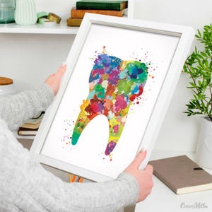 May include: A framed print featuring a colorful watercolor illustration of a tooth. The tooth is depicted with vibrant splashes of red, blue, green, yellow, and purple. The artwork is set against a white background within a white frame.