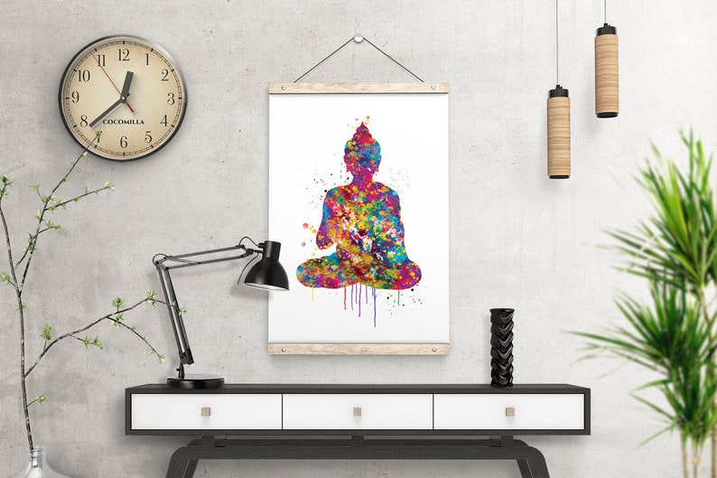 May include: A colorful watercolor print of a seated Buddha figure. The artwork features a vibrant mix of colors, including blues, greens, yellows, and reds, creating a striking visual effect. The print is displayed on a white background and framed with wooden bars.