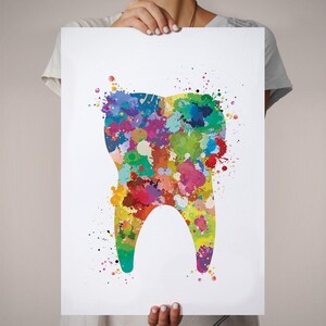 May include: A colorful watercolor print of a tooth. The tooth is filled with vibrant paint splatters in shades of red, yellow, green, blue, and purple. The artwork is held by a person.