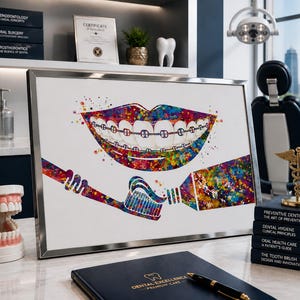 Puede incluir: Una impresión en acuarela enmarcada que representa una boca sonriente con brackets, un cepillo de dientes y pasta dental. La obra de arte utiliza un efecto de salpicadura colorido. También se ven artículos relacionados con la odontología.