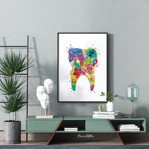 May include: A framed watercolor print of a tooth, featuring a colorful splatter design. The artwork is displayed on a wall above a green cabinet with decorative items. The overall theme is dental art.