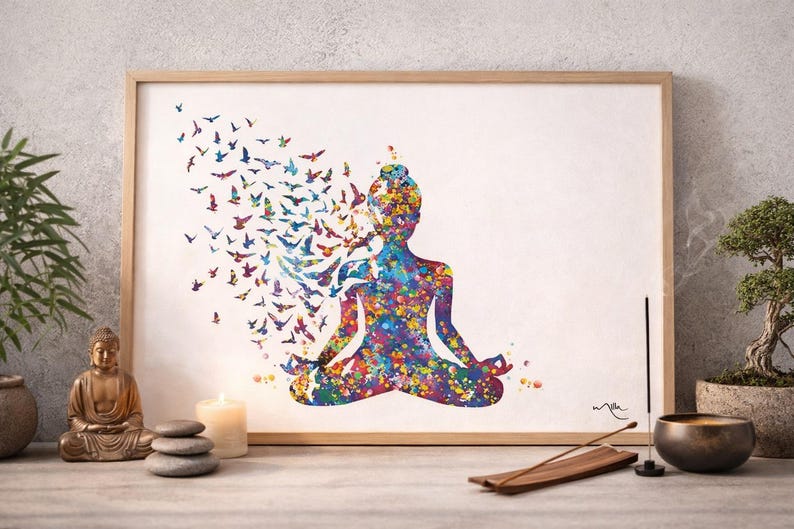 May include: A framed art print shows a colourful watercolour silhouette of a person in a yoga pose, with birds emerging from the head. The artwork features a vibrant palette of blues, purples, and yellows. The print is displayed on a table with a Buddha statue and a lit candle.